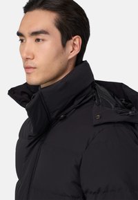 Must tumeroheline jope kõrge kraega, varustatud lukudega, nupuklippidega ja siledast tekstuurist. Kujundus on struktureeritud ja kaasaegne.