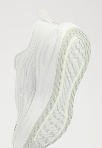Chaussure de sport blanche avec semelle texturée et logo Nike swoosh, inclinée pour mettre en valeur la semelle et le profil latéral.