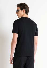 Camiseta negra de manga corta hecha de algodón con un corte relajado. Textura suave, diseño minimalista y cuello redondo clásico. Sin logotipos visibles.