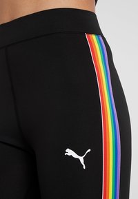 Leggings de sport noirs avec une bande arc-en-ciel colorée sur le côté et un logo Puma blanc sur le bas de la jambe. Tissu lisse et extensible.