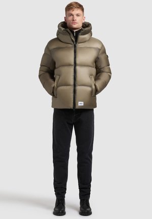 Puffjacka i olivgrön, med huva, quiltat mönster, framdragkedja och sidofickor. Matchas med svarta jeans och stövlar.