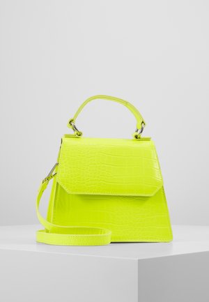 Borsa a mano di un vivace giallo neon con texture effetto coccodrillo, dotata di manico superiore e tracolla regolabile, posata su una superficie bianca.