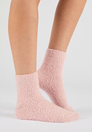 Jambes portant des chaussettes douces, moelleuses, rose clair jusqu'à la cheville sur un fond clair uni.