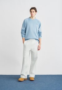 Ανοιχτό γαλάζιο φούτερ με V-λαιμόκοψη και κεντημένο λογότυπο· συνδυάζεται με εκρού παντελόνι φούτερ με πλαϊνές ραφές· καφέ τσόκαρα.