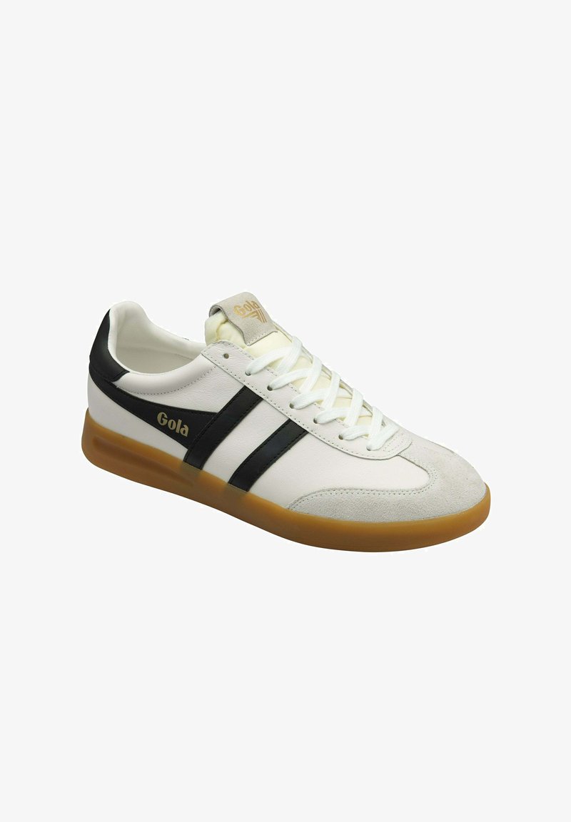 Witte sneaker met zwarte strepen en een tan rubberen zool. Heeft een suède neus, ronde veters en "Gola" branding aan de zijkant en op de tong.
