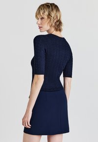 Navy gestricktes Oberteil mit strukturiertem Muster, kurzen Ärmeln und taillierter Passform, kombiniert mit einem passenden navy Rock.