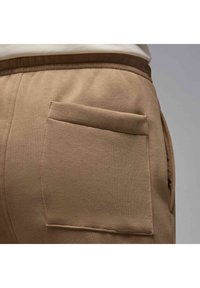 Beige joggers with a textured fabric, featuring a single rear patch pocket and an elastic waistband for comfort.