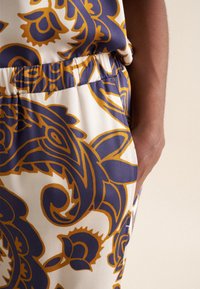 Pantaloni da donna con un vivace motivo paisley in blu navy e senape su sfondo crema, dotati di una vita elasticizzata e tasca laterale.