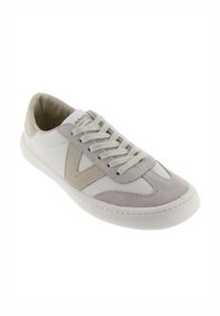 Zapatilla blanca y gris hecha de cuero y ante, con cierre de cordones, puntera texturizada y diseño lateral en contraste.