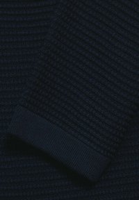 Navyblå tröja i waffle-stickad tyg med ribbad manschettdetalj; texturen verkar mjuk med varierande mönster från stickdesignen, vilket skapar visuell intressant.