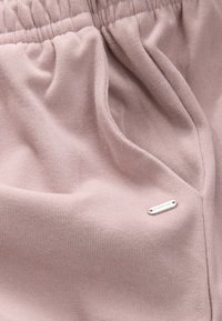 Light pink fabric with a ribbed texture, featuring an elastic waistband and a small metallic tag labeled "DOWNTIME" on the side.