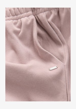 Svijetloružičasta tkanina s rebrastom teksturom, s elastičnim pojasom i malom metalnom oznakom s natpisom "DOWNTIME" sa strane.