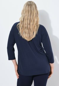 Tummansininen, pitkähihainen paita rentoa istuvuutta, kaareva helma ja pehmeä rakenne, yhdistettynä vastaaviin tummansinisiin leggingseihin.