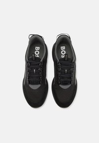 Chaussures de sport noires en mesh et suède, dotées d'une tige texturée, de lacets et d'une semelle en caoutchouc. Logo visible sur les semelles intérieures.