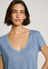 Gaiši zils V veida kakla T-krekls ar īsām piedurknēm. Mīksta, teksturēta auduma, ar kontrastējošu vieglāku zilu apkakli. Smalks logo uz priekša.