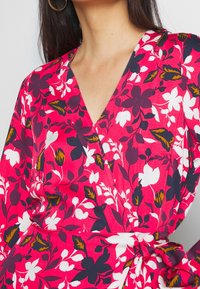 Abito floreale avvolgente con scollatura a V profonda e maniche a ¾. Realizzato in tessuto leggero, presenta vivaci motivi floreali in rosa, bianco e viola scuro.