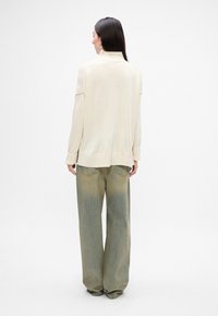 Maglione lavorato a maglia color beige chiaro con colletto alto, polsini a coste e vestibilità rilassata, abbinato a pantaloni in denim verde chiaro e svasati.