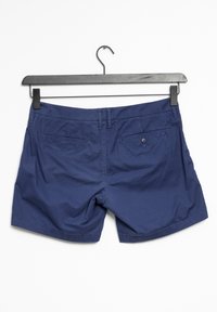 Marinblå bomullsshorts hängande på en svart galge, med midjeband, två bakfickor med knappar och en ren, slät yta.