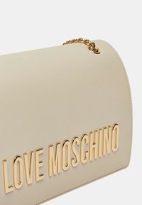 Borsa sintetica beige con una superficie liscia, caratterizzata da bold lettering "LOVE MOSCHINO" dorato e un accentuazione con catena dorata.
