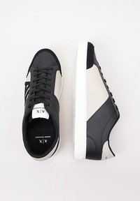 Zapatillas de cuero en negro y crema con una textura suave, que cuentan con una suela de goma blanca, cordones planos y sutiles acentos de diseño en los laterales.