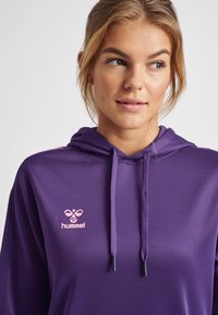 Paarse hoodie met een trekkoord in de capuchon, zachte textuur en een roze "hummel" logo op de borst, met roze accenten op de schouders.