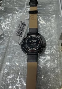 Zwarte leren horlogeband met een ronde kast van roestvrij staal. Heeft een zwarte wijzerplaat met witte en rode markeringen. Achterkant gemarkeerd met "designed by Regal Sweden."