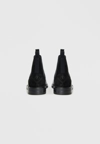 Black suede ankle boots with elastic side panels, reinforced heel, and flat rubber sole. Notable embossed logo on back.