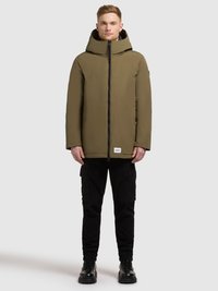 Olivgrön huva jacka med dragkedja och svarta detaljer, bärs över svarta cargobyxor och robusta svarta stövlar. Minimalistisk design.