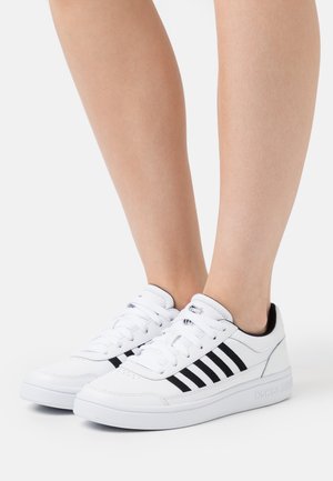 Sneakers bianchi con strisce nere, design con lacci, suola in gomma e collo imbottito. Realizzati in materiale sintetico, presentano una texture liscia.
