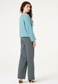 Hellblauer gestrickter Pullover mit lässigem Schnitt, kombiniert mit hoch taillierten weit geschnittenen Hosen in Schwarz-Weiß mit geometrischen Mustern.