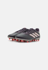 Botas de fútbol en negro y gris con una superficie texturizada, que presentan tres franjas blancas y picos rojos en la suela para tracción.