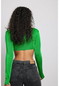 Long-sleeved, cropped top in bright green ribbed fabric, paired with high-waisted dark grey jeans featuring a tan brand tag on the back.