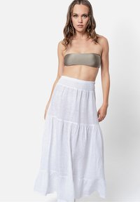 Gonna maxi bianca a strati realizzata con tessuto leggero, caratterizzata da una vita arricciata. Indossata con un top bandeau verde oliva.