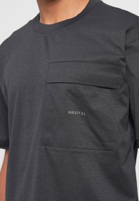 Mørkegrå kortærmet t-shirt med en stor brystlomme med klap og lille hvid "Oakley F.G.L" tekst på fronten.