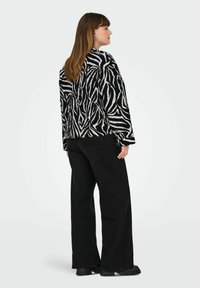 Juoda ir balta dryžuota striukė su minkšta tekstūra, turinti laisvą siluetą ir ilgas rankoves, derinama su aukštai supjaustytomis juodomis plačiomis kelnėmis.