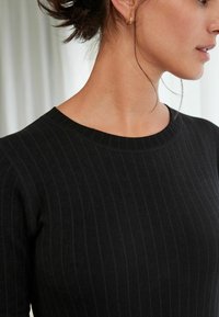 Top de punto negro con canalé que presenta un escote redondo y rayas verticales, destacado por una textura suave y una silueta ajustada.