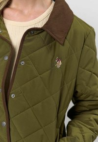 Zelená prešívaná bunda s diamantovým vzorom, hnedý kordový golier, kovové cvoky a malý vyšitý detail.