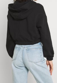 Sweatshirt noir court avec capuche, doté de poignets et d'un ourlet élastiqués. Associé à un jean bleu clair taille haute, présentant des détails d'usure minimes.