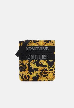 Schwarze Umhängetasche mit kunstvollem goldenem Barockmuster, schwarzem Riemen und weißem Schriftzug "Versace Jeans Couture" auf der Vorderseite.