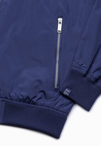 Marinblå bomberjacka i ett mjukt och lätt material med elastiska muddar, silverfärgad dragkedja och en liten etikett på mudden.