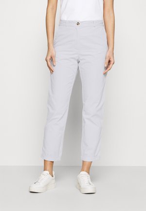 Pantalon blanc court décontracté porté avec des baskets blanches et une chemise blanche, montré du milieu du torse jusqu'aux pieds sur un fond uni.