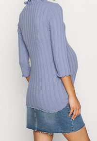 Ljusblå ribbad topp med en volangkant och 3/4 ärmar, kombinerad med en trasig denimkjol. Tyget har en mjuk textur och lätt stretch.