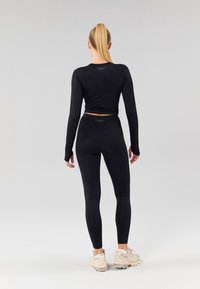 Zwarte lange mouwen top en strakke leggings van rekbaar materiaal, met een hoge tailleband, naadloos ontwerp en subtiele branding op de achterkant.