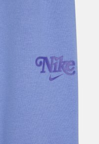 Una tela de color azul claro presenta un prominente logo de Nike en púrpura, exhibiendo una textura suave y un diseño simple sin patrones adicionales.