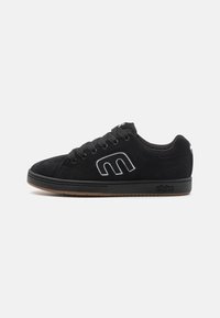 Black suede skate shoes with lace-up closure, white logo detailing on the side, and a gum rubber outsole. Low-top design.