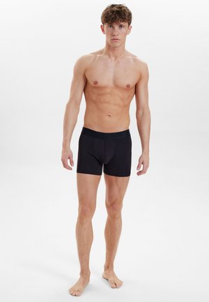 Sorte bomuldsboxershorts med en fleksibel talje, der sidder tæt omkring lårene, præsenteret på en model med en atletisk bygning.