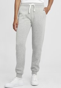 Grå joggingsbyxor i mjukt tyg, med dragsko i midjan, sidofickor och smalnade mudd vid anklarna. Matchas med vita sneakers.