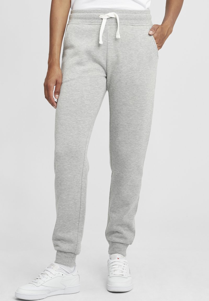 Grå joggingsbyxor i mjukt tyg, med dragsko i midjan, sidofickor och smalnade mudd vid anklarna. Matchas med vita sneakers.