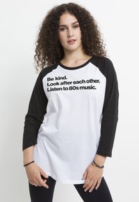 Zwart-witte honkbal T-shirt met driekwartmouwen. Bevat gedrukt tekst in vetgedrukt zwart lettertype op het witte voorpaneel.