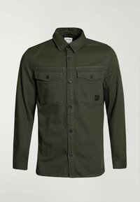 Chemise à manches longues vert foncé avec deux poches poitrine, un col, et un petit patch de logo noir sur la poche droite.